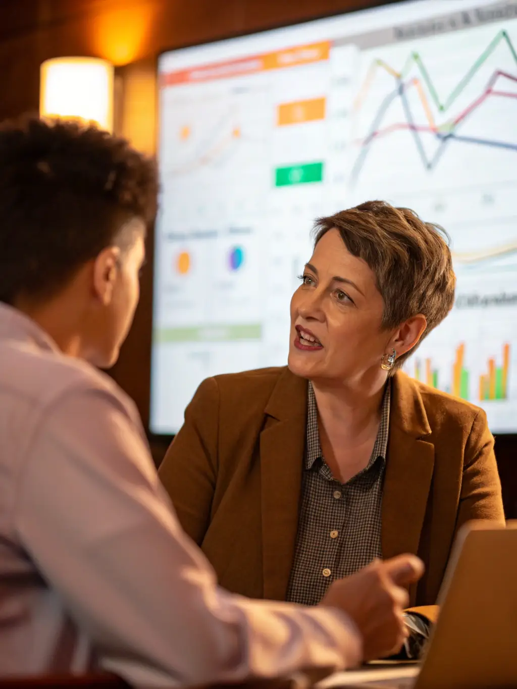 An image of a financial advisor discussing investment options with a client, with graphs and charts in the background, representing mechanicgate.uno's investment planning service.